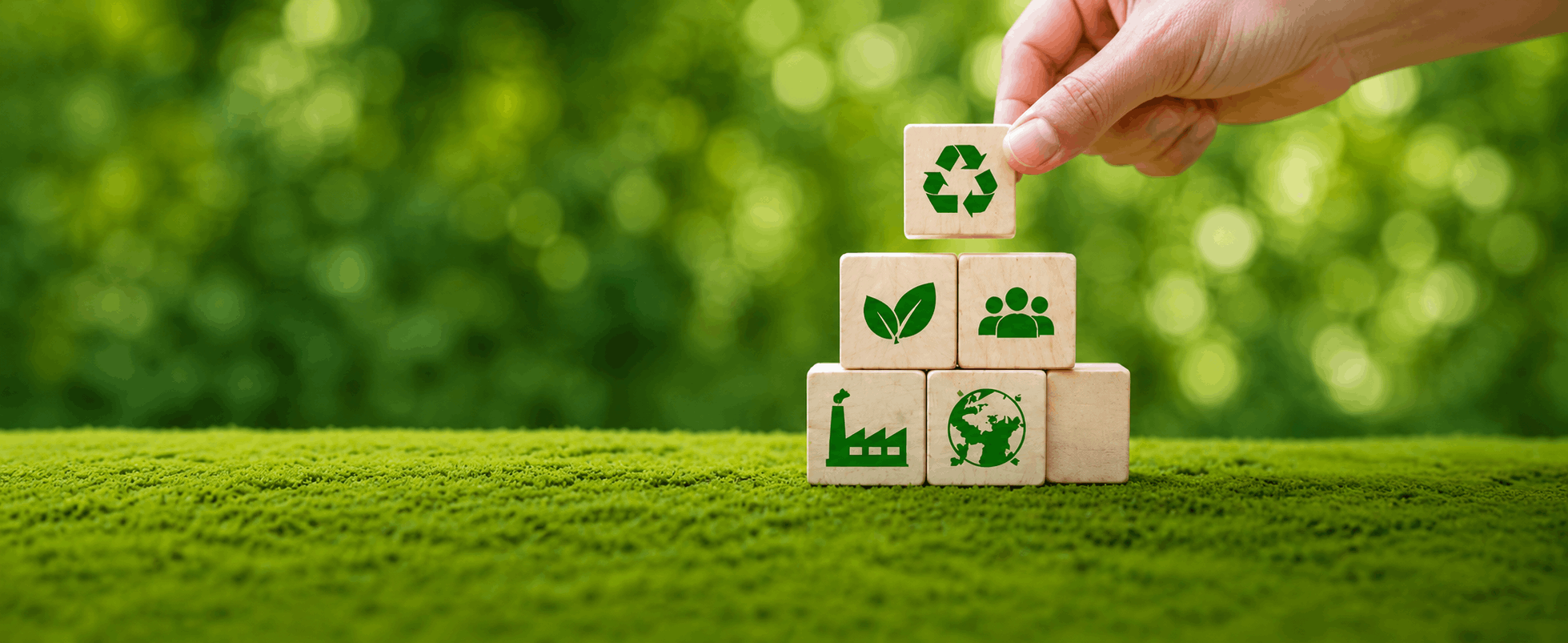 Bannière illustrant des critères environnementaux et sociaux avec des cubes en bois portant des symboles écologiques et une main plaçant un bloc recyclage.